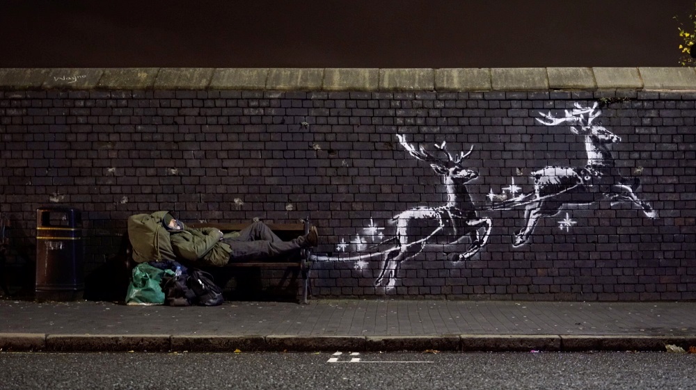 A man lays on a bench next to a new mural by Banksy in Birmingham, Britain, December 9, 2019, in this picture obtained from social media. u00e2u20acu201d @banksy/Instagram via Reuters  