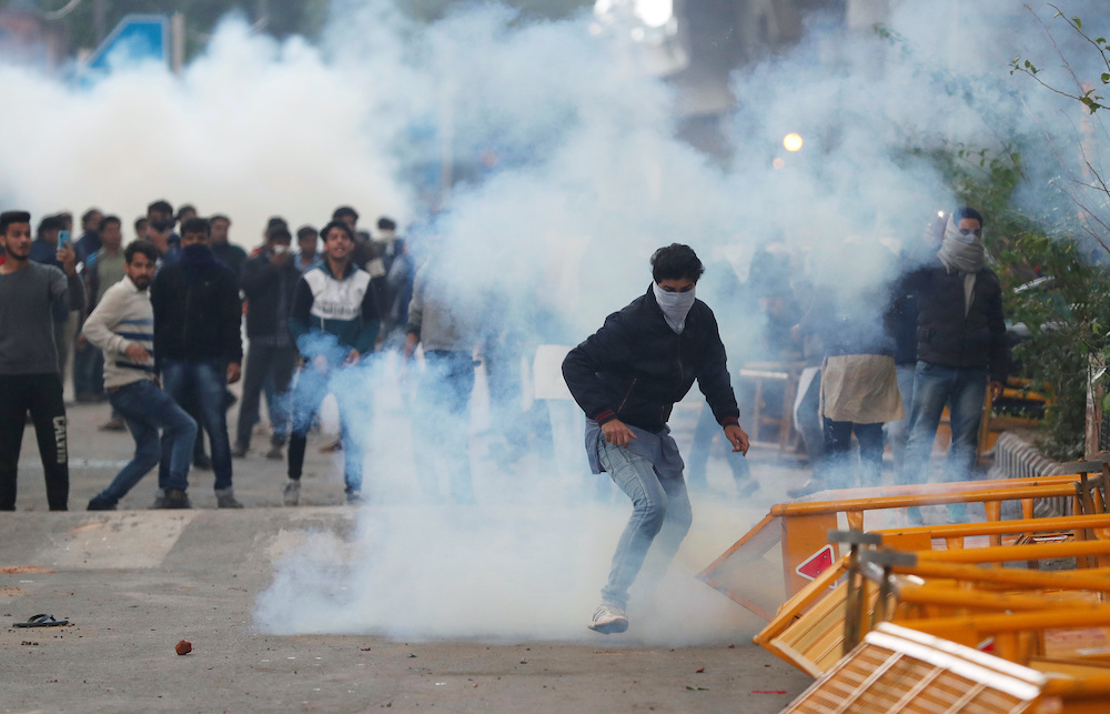Protesters run for cover amid tear gas fired by police during a protest against the Citizenship Amendment Bill, a bill that seeks to give citizenship to religious minorities persecuted in neighbouring Muslim countries, outside the Jamia Millia Islamia Uni