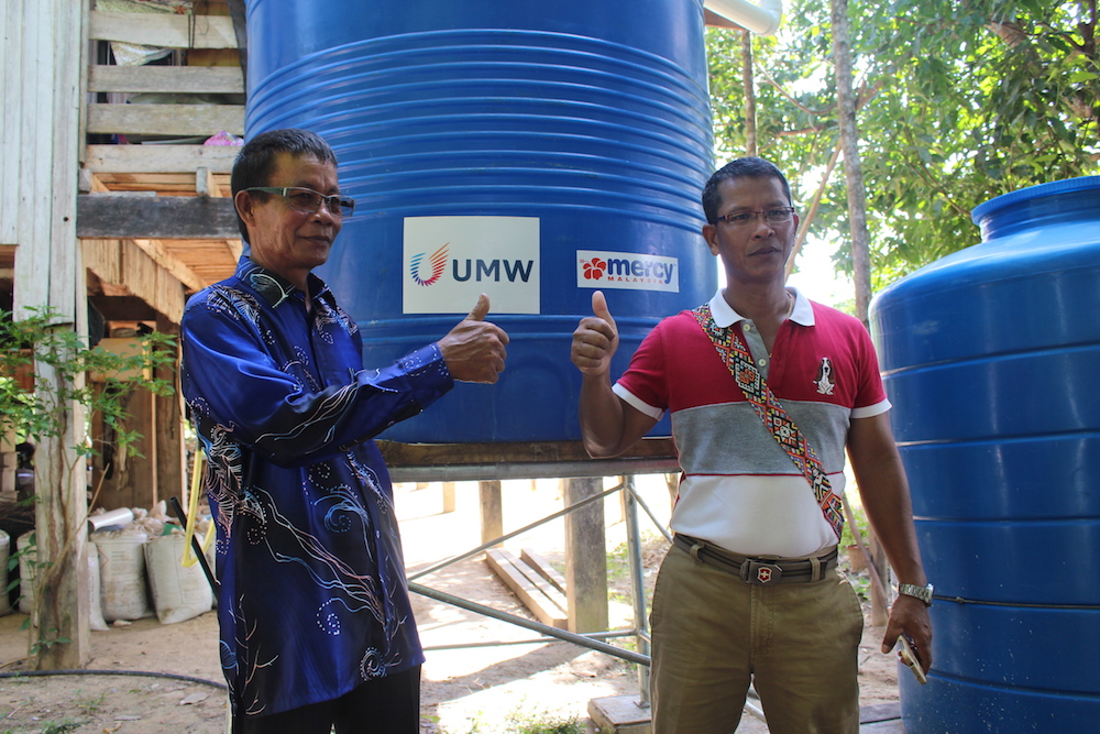 Marius Mokinson (right) and village head Juslee Bokoot with one of the newly installed tanks at a home in Kampung Suang Duyung, Pitas. u00e2u20acu201d Picture by Julia Chan