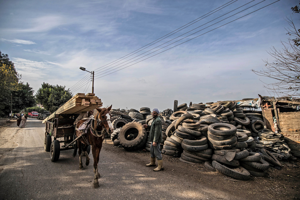 A labourer stands before piles of stacked tyres as a horse-drawn cart carrying wooden beams passes by, at a rubber recycling workshop in the village of Mit al-Harun in Egypt's central Nile delta Gharbia Governorate. u00e2u20acu201d AFP pic