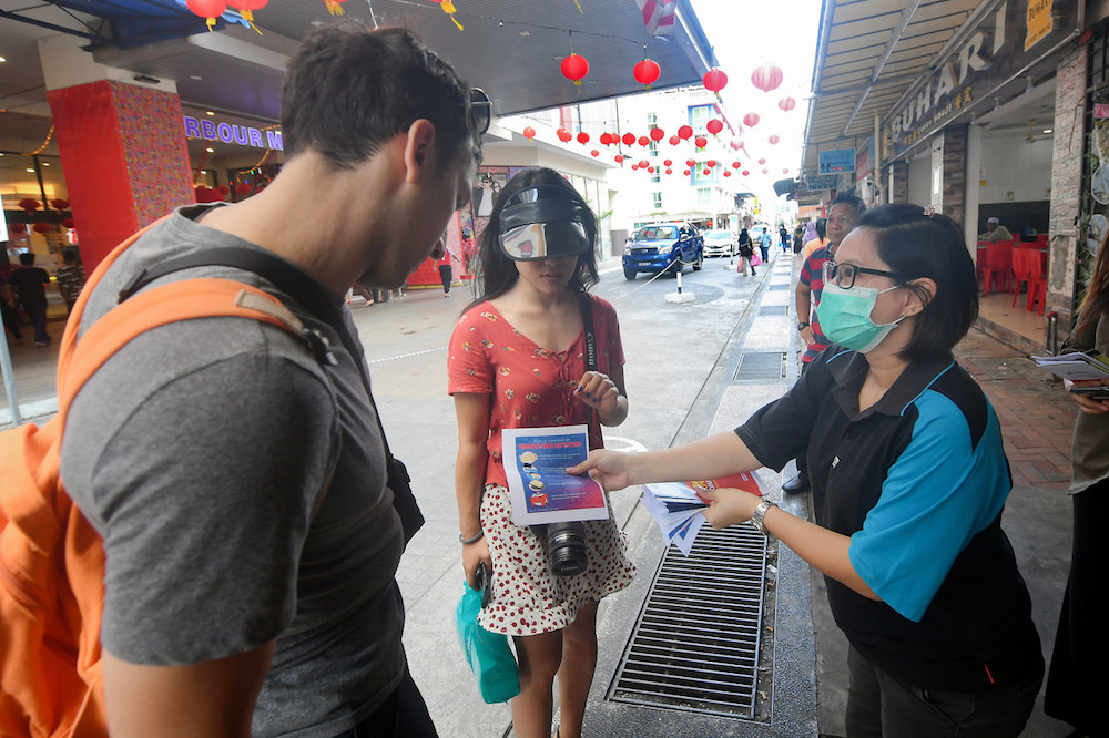 A Sandakan Information Department staff distributes leaflets on the 2019 novel coronavirus infection to tourists in Sandakan January 30, 2020. u00e2u20acu201d Bernama pic