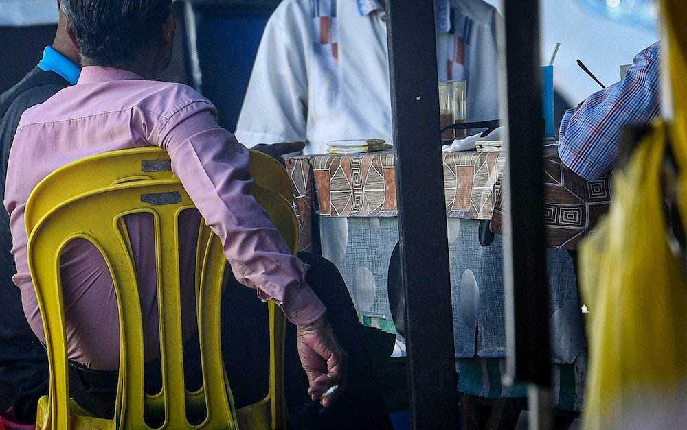 A man attempts to conceal his cigarette as health officers approach his table during an inspection at an eatery in Medan Selera Jalan Raja Muda Abdul Aziz in Kuala Lumpur January 1, 2020. u00e2u20acu201d Bernama pic