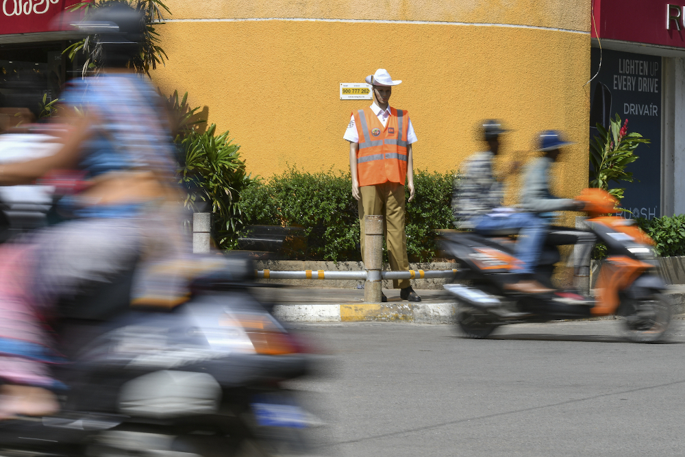 Motorists ride past a mannequin dressed up as traffic police at an intersection in Bangalore. u00e2u20acu201d AFP pic