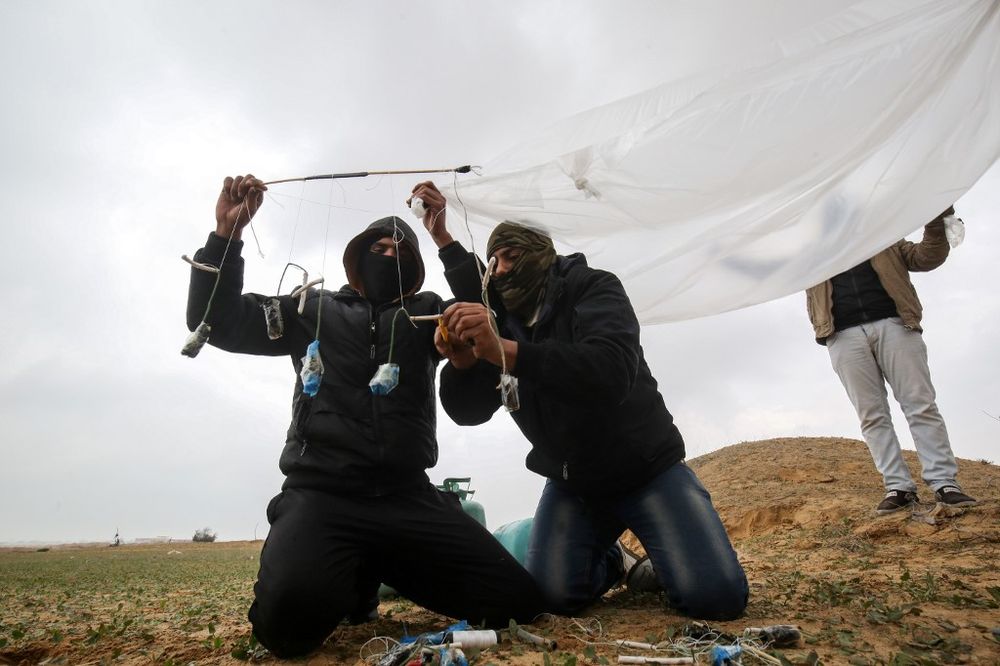 Young Palestinian men, masked in order to avoid being recognised, prepare a flammable object to be flown toward Israel, near the Israel-Gaza border east of Rafah in the southern Gaza Strip, on January 18, 2020. u00e2u20acu201d AFP pic