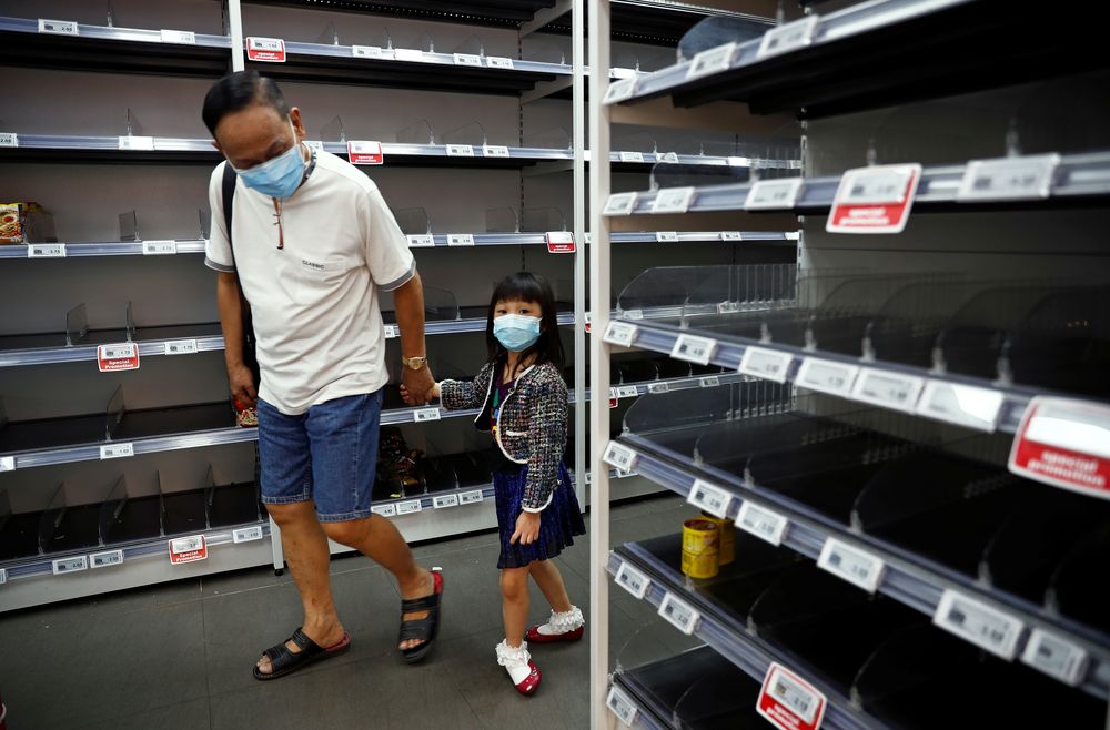 A man and a child wear protective masks, looking at empty shelves of canned food and instant noodles as people stock up on food supplies, after Singapore raised coronavirus outbreak alert level to orange, at a supermarket in Singapore February 8, 2020. u00e2u20ac