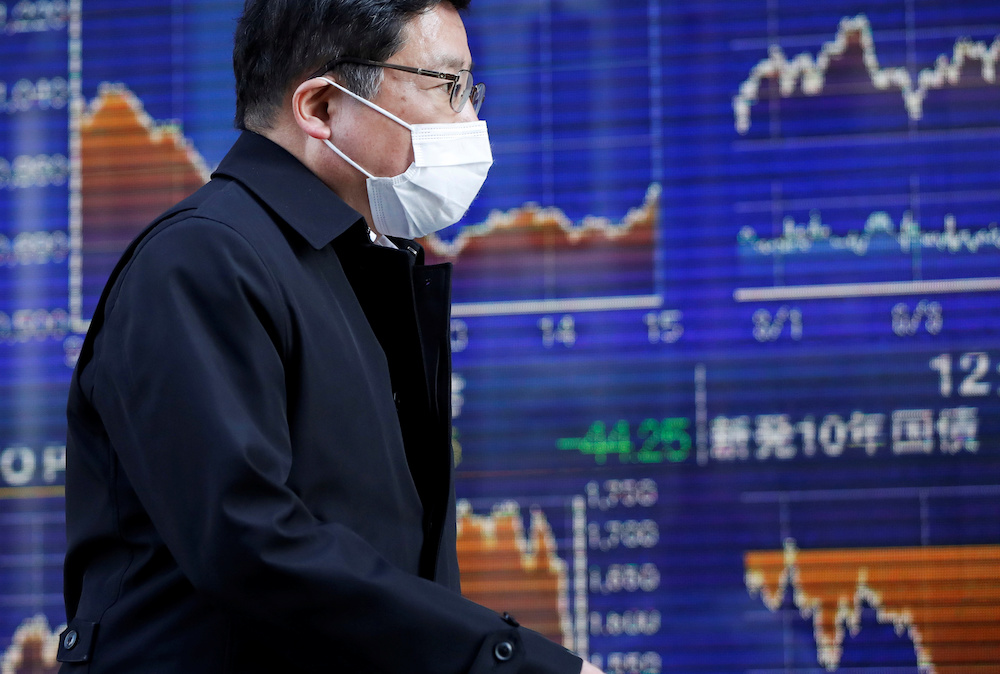 A passerby wearing a protective face mask walks past an electronic board showing the graphs of the recent movements of Japan's Nikkei share average outside a brokerage in Tokyo March 6, 2020. u00e2u20acu201d Reuters pic