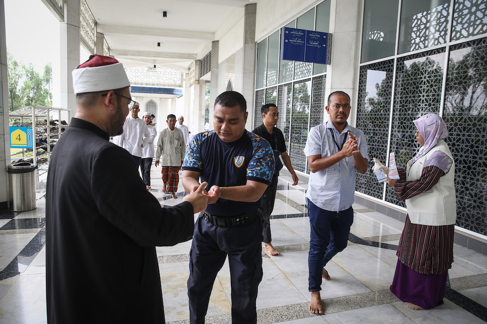 Staff member from mosque distributes hand sanitiser to worshippers during Friday prayers at Sultan Salahuddin Abdul Aziz Shah Mosque in Shah Alam March 13, 2020. u00e2u20acu201d Picture by Yusof Mat Isa