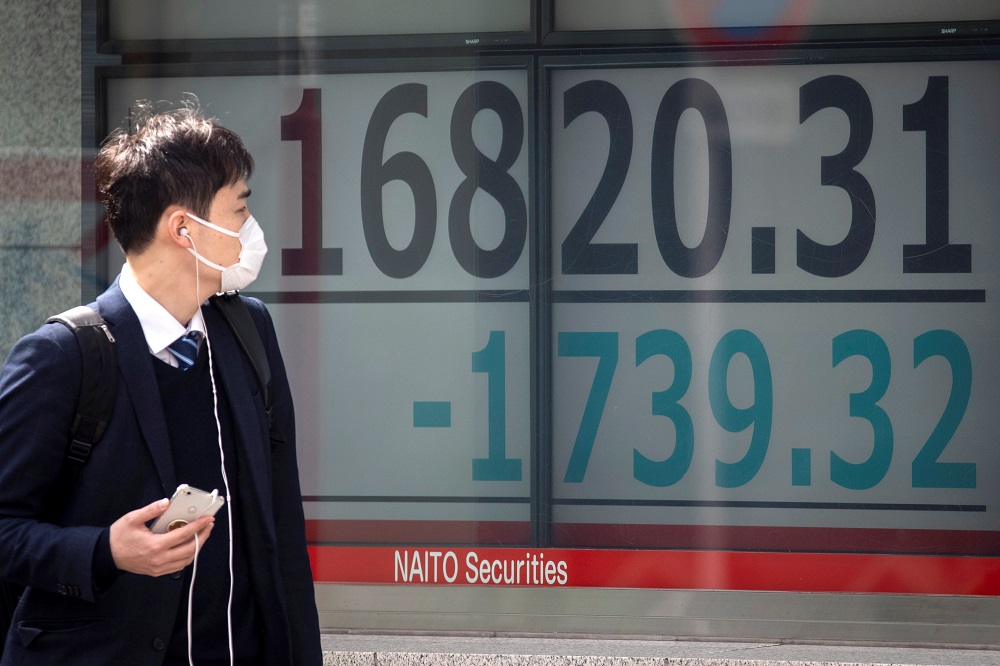 A man wearing a protective face mask walks past a screen showing the Nikkei index outside a brokerage in Tokyo March 13, 2020. u00e2u20acu201d Reuters pic