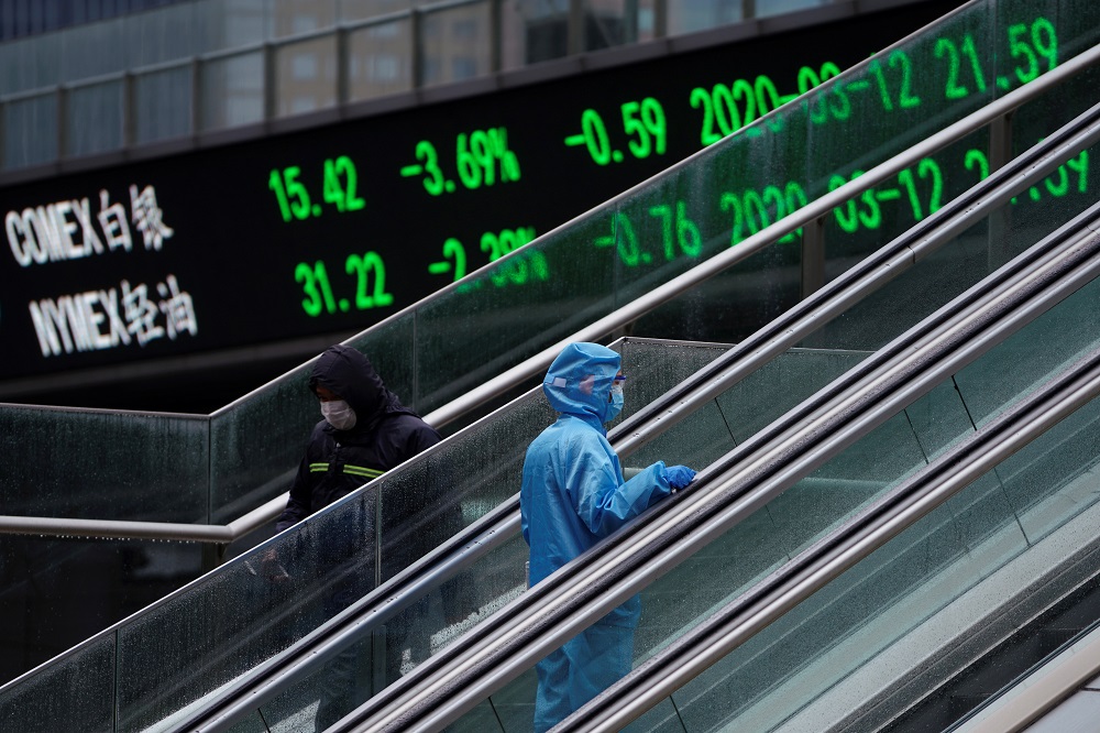 A pedestrian in protective suit rides an escalator near an overpass with an electronic board showing stock information at Lujiazui financial district in Shanghai March 13, 2020. u00e2u20acu201d Reuters pic
