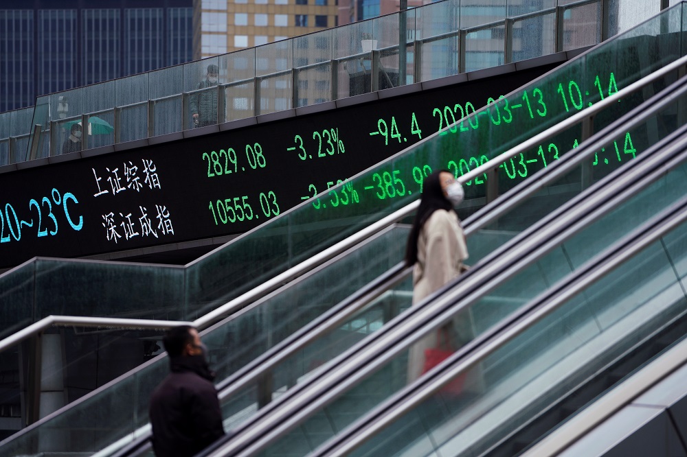 Pedestrians wearing face masks ride an escalator near an overpass with an electronic board showing the Shanghai and Shenzhen stock indexes at Lujiazui financial district in Shanghai March 13, 2020. u00e2u20acu201d Reuters pic