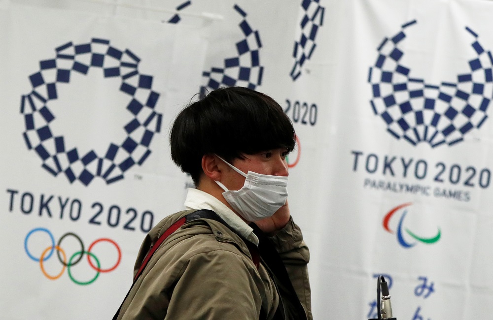 A man wearing a protective face mask, following an outbreak of Covid-19, walks in front of flags of the Tokyo 2020 Olympic and Paralympic Games in Tokyo March 17, 2020. u00e2u20acu201d Reuters pic