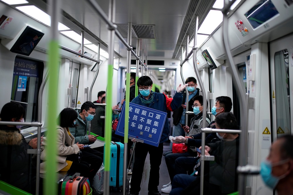 A staff member wearing a face mask holds a placard while standing among passengers on a subway train, on the first day the city's subway services resumed following the novel coronavirus disease outbreak in Wuhan March 28, 2020. — Reuters pic