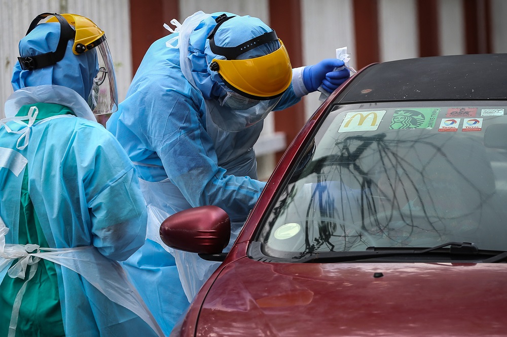 A health worker in protective suit swabs a driveru00e2u20acu2122s mouth at a drive-through testing site for Covid-19 at KPJ Damansara Specialist Hospital in Petaling Jaya March 28, 2020. u00e2u20acu201d Picture by Yusof Mat Isa