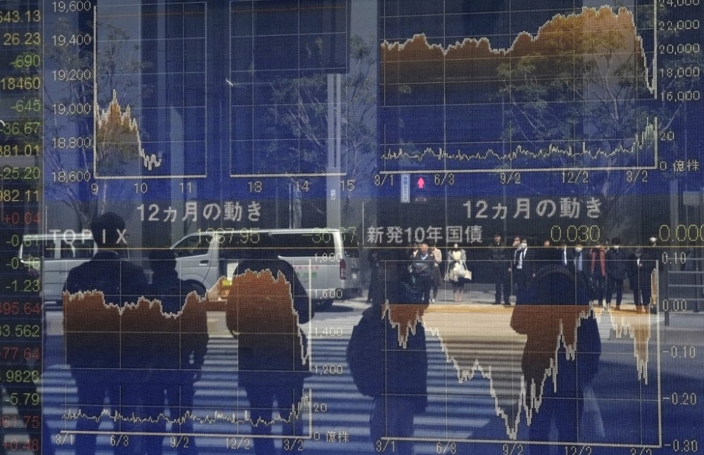 Pedestrians reflected in a window stand in front of a quotation board displaying the numbers on the Tokyo Stock Exchange March 26, 2020. u00e2u20acu201d AFP pic