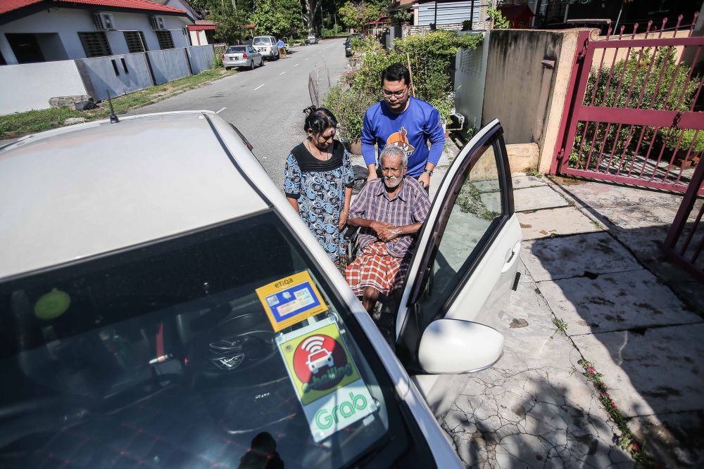 Former Kosmo! Perak bureau chief Mohamad Tarmize Mohd Nor (in blue) helps Vanaja Suppiah (left) wheel her husband to their ride in Ipoh March 26, 2020. u00e2u20acu201d Picture by Farhan Najib