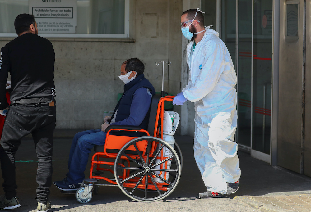 A healthcare worker wearing a protective face mask and suit pushes a patient in a wheelchair near the emergency unit at 12 de Octubre hospital during the coronavirus disease (Covid-19) outbreak in Madrid, Spain March 28, 2020. u00e2u20acu201d Reuters picnn