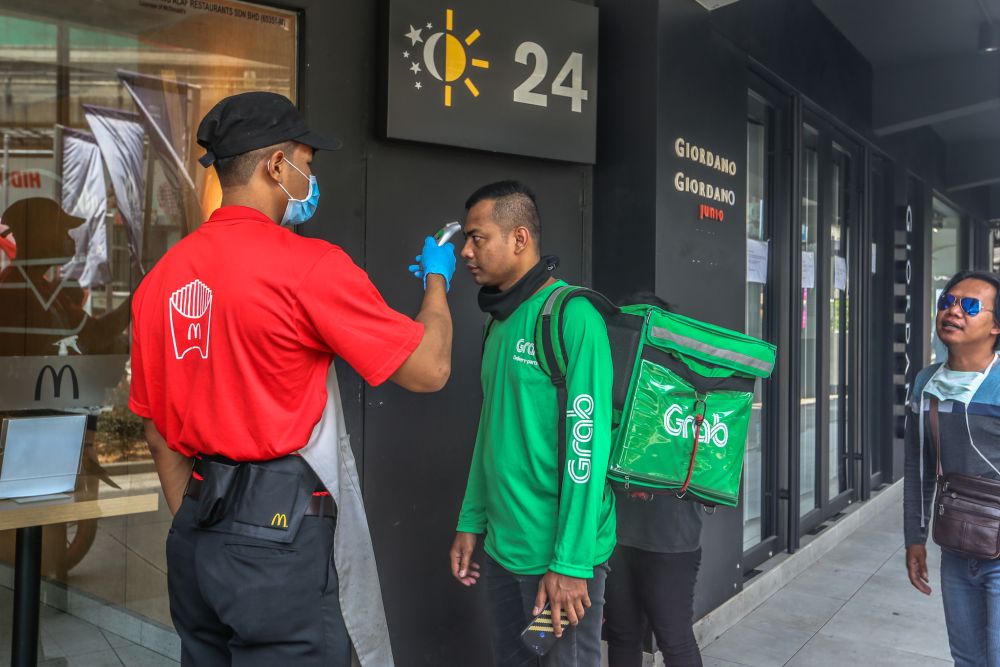 A GrabFood rider is screened by a McDonaldu00e2u20acu2122s staff in Bukit Bintang as the movement control order kicks in on March 18, 2020. u00e2u20acu201d Picture by Firdaus Latif