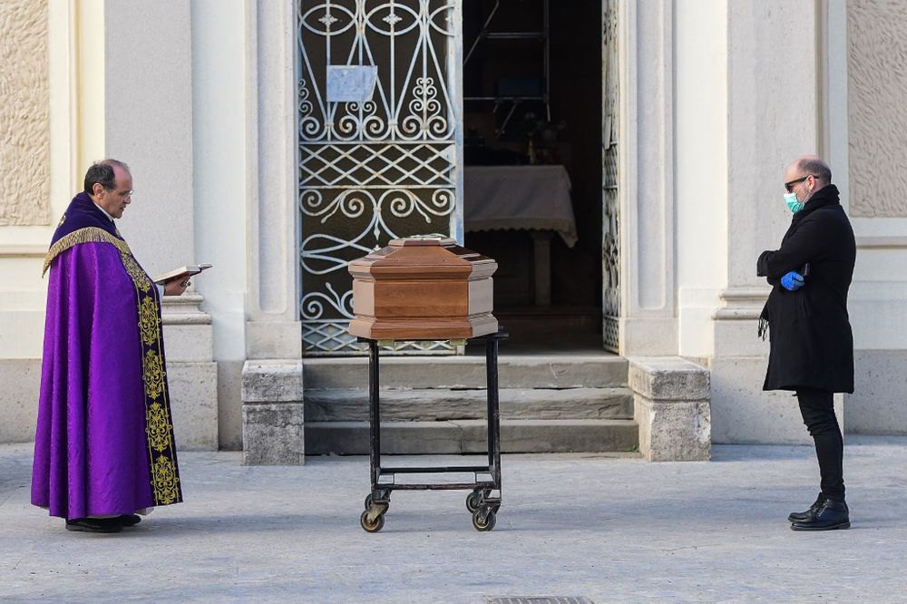 A man wearing a face mask stands by the coffin of his mother as a priest reads prayers during a funeral service in the closed cemetery of Seriate, near Bergamo, Lombardy, on March 20, 2020. u00e2u20acu201d AFP pic