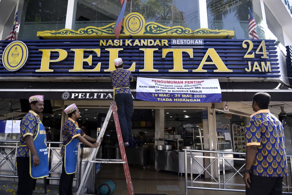 A Pelita Nasi Kandar worker hangs up a sign detailing the dine-in restriction in Bangsar March 18, 2020. u00e2u20acu201d Picture by Miera Zulyana
