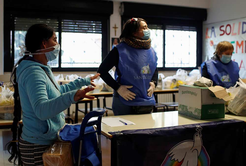 A woman and volunteers wearing protective face masks and gloves attend to food distribution organised by the Sant'Egidio Community at the San Gaudenzio parish during the Covid-19 lockdown in Rome, Italy, March 23, 2020. u00e2u20acu201d Reuters pic