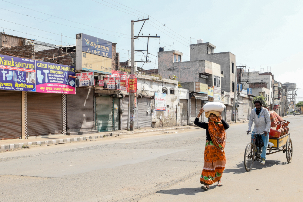 A woman carries a sack of wheat flour on her head as a man rides a three-wheeler cart loaded with gas cylinders on a deserted street during a government-imposed nationwide lockdown as a preventive measure against the Covid-19 coronavirus in Amritsar March