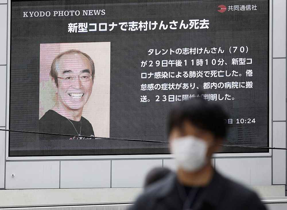 A man wearing a protective face mask walks past a huge screen reporting the death of Japanese comedian Ken Shimura, who had been infected with Vovid-19, in Osaka, Japan March 30, 2020. u00e2u20acu201d Kyodo pic via Reuters