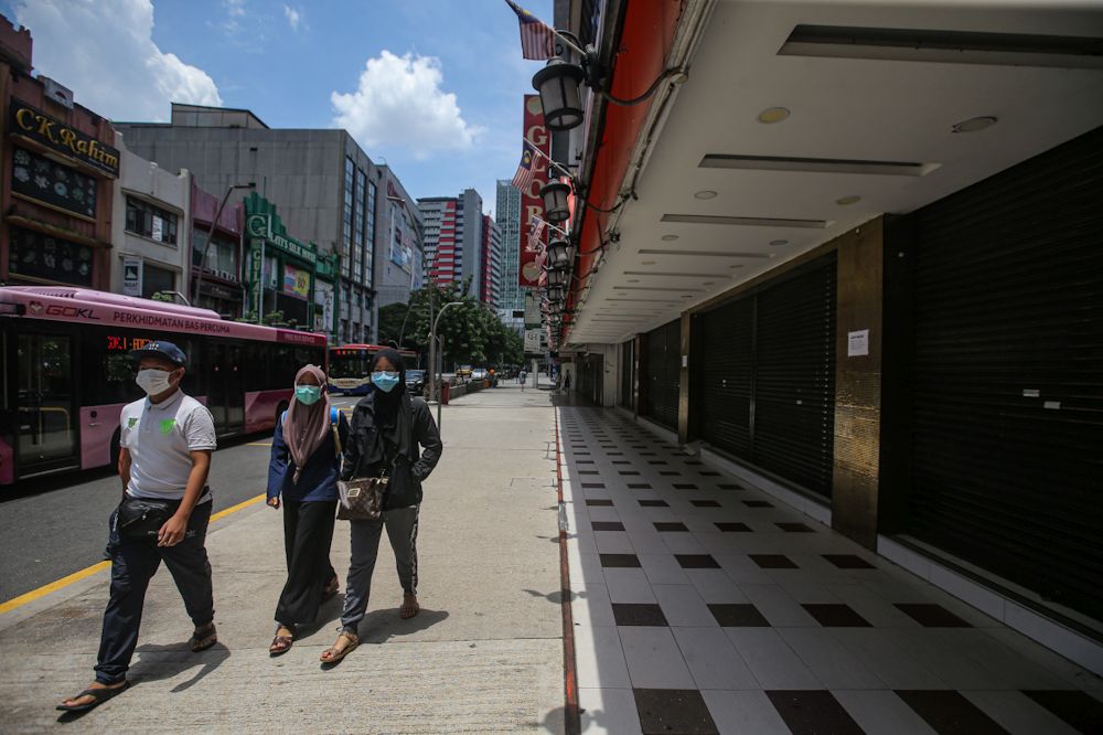 People wearing face masks walk past shuttered shops along Jalan Tuanku Abdul Rahman as the movement control order kicks in on March 18, 2020. u00e2u20acu201d Picture by Hari Anggara