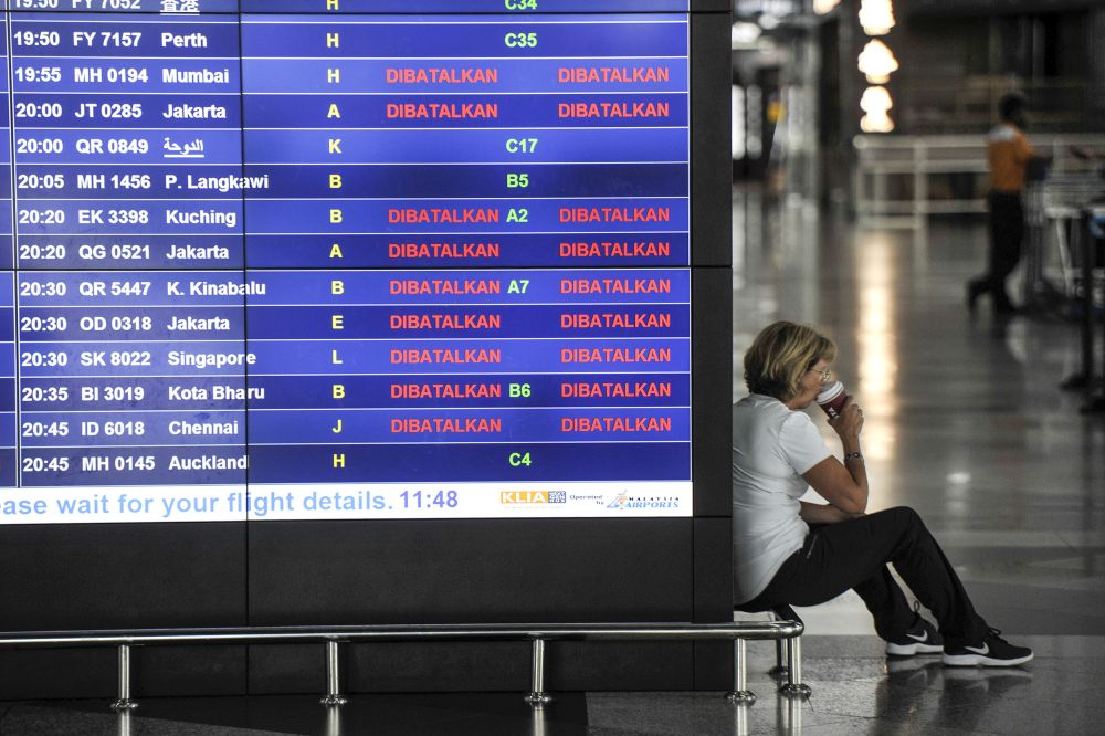 A woman sips on cup of coffee next to a flight information screen at the Kuala Lumpur International Airport in Sepang March 18, 2020. u00e2u20acu201d Picture by Shafwan Zaidon