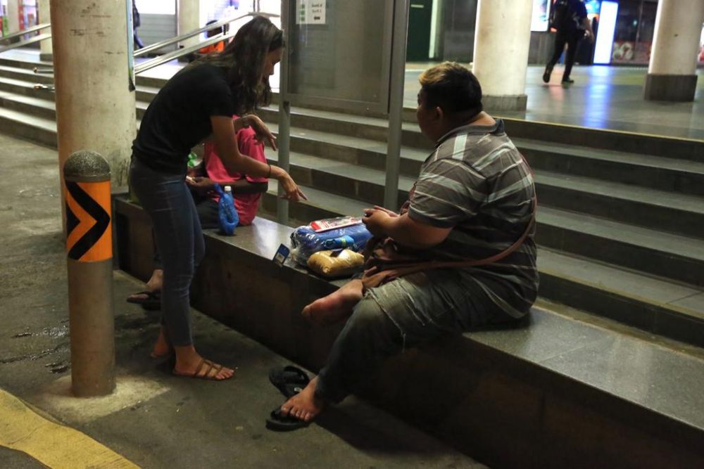 A volunteer is seen handing out items to two Malaysian workers at a bus stop outside Kranji MRT Station on March 19, 2020. u00e2u20acu201d TODAY pic