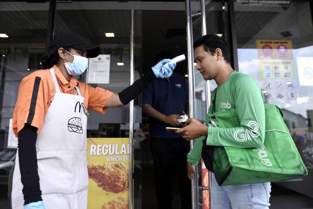 A GrabFood rider is screened by a McDonaldu00e2u20acu2122s staff in Bangsar as the movement control order kicks in on March 18, 2020. u00e2u20acu201d Picture by Miera Zulyana