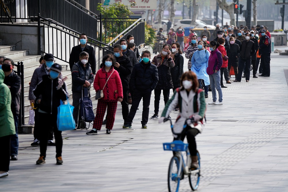 A woman wearing a face mask rides a shared bicycle past people lining up to enter a supermarket in Wuhan April 1, 2020. u00e2u20acu201d Reuters pic