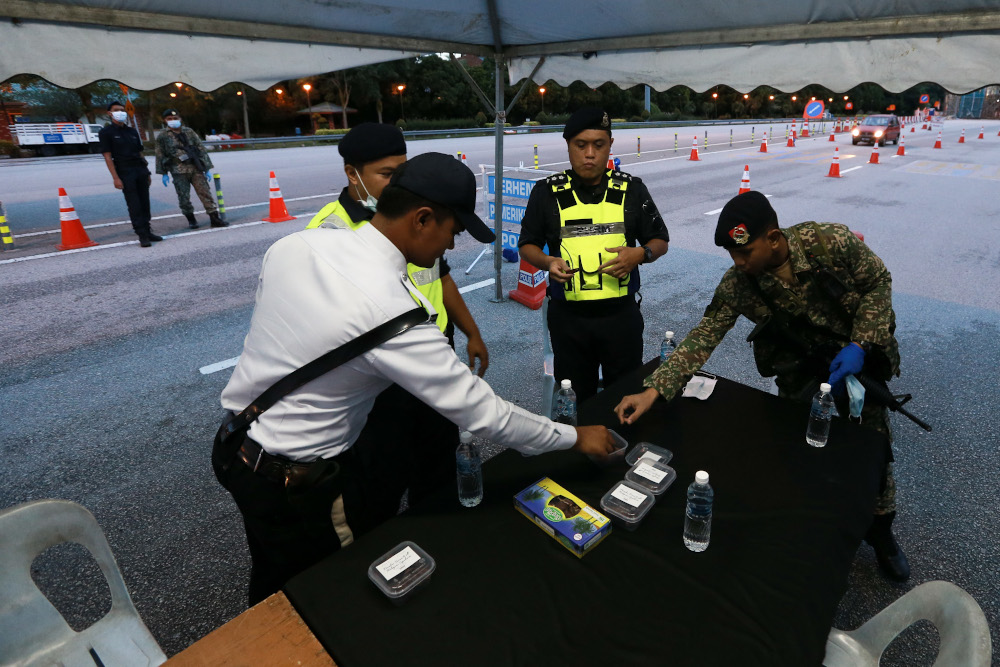 Police and armed forces personnel break fast with dates and mineral water as they inspect vehicles going through the roadblock during the movement control order April 24, 2020. u00e2u20acu201d Picture by Ahmad Zamzahuri