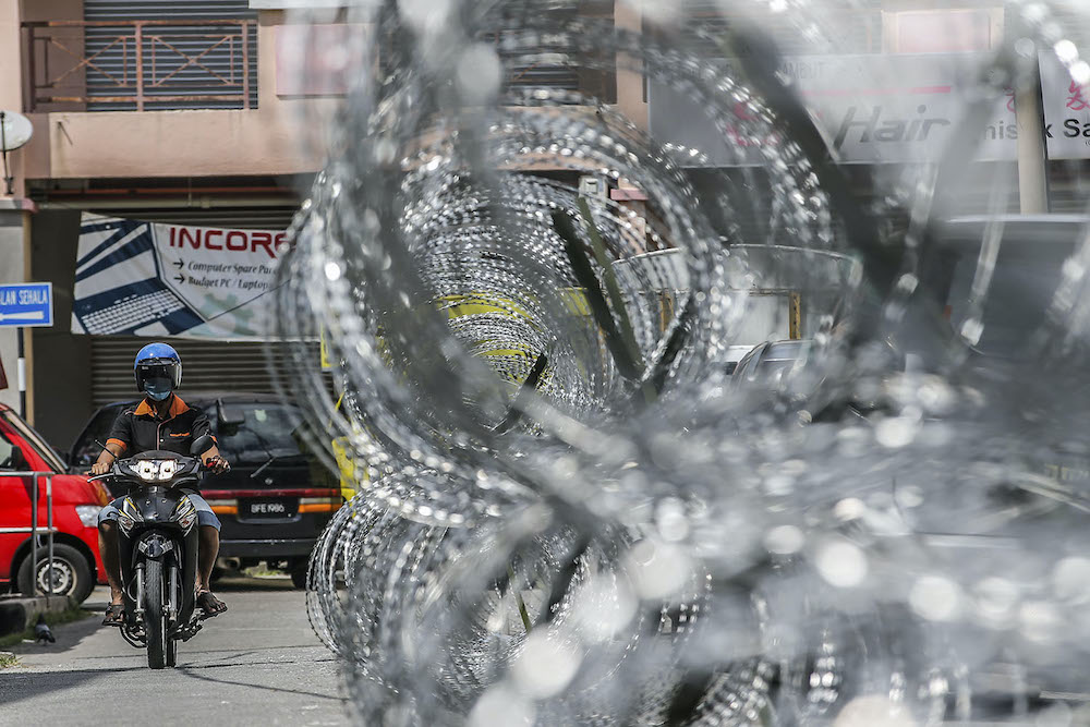 A motorcyclist rides past barbed wire fencing in Selayang Baru, amid the enhanced movement control order April 25, 2020. u00e2u20acu2022 Picture by Hari Anggara