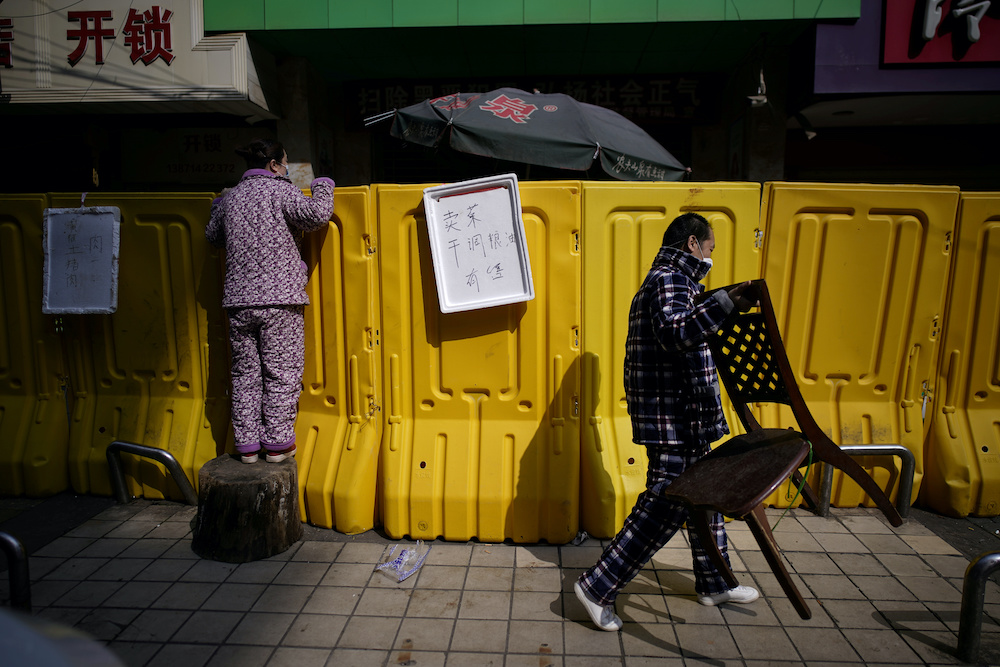 A resident pays for groceries by standing on a tree stump to peer over barriers set up to ring fence a wet market on a street in Wuhan, Hubei province, the epicentre of China’s coronavirus disease (Covid-19) outbreak, April 1, 2020. — Reuters pic