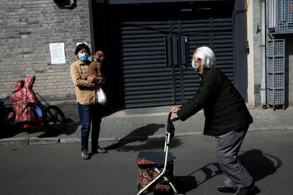 A woman wearing a face mask observes a moment of silence while holding her dog in Beijing, as China holds a national mourning for those who died of the coronavirus disease (Covid-19), on the Qingming tomb-sweeping festival, April 4, 2020. u00e2u20acu201d Reuters pic