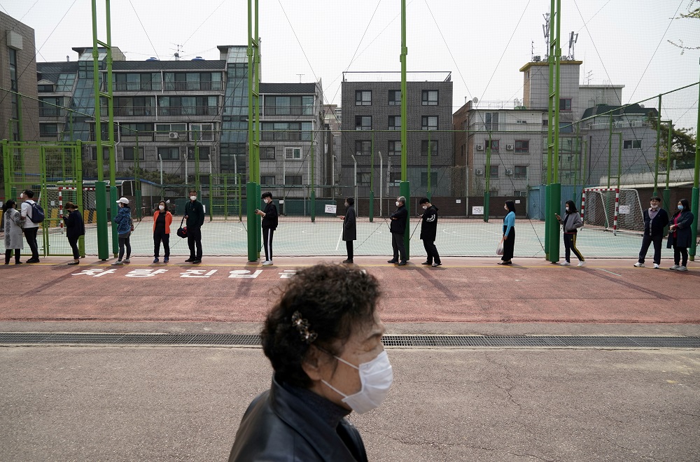 A woman walks past a queue of voters wearing masks, in an effort to prevent the spread of the coronavirus disease, while waiting to cast their ballots at a polling station in Seoul April 15, 2020. u00e2u20acu2022 Reuters pic