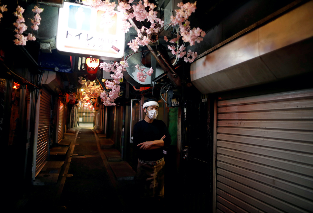 A staff member of a restaurant wearing a protective face mask stands at almost empty and temporary closed Japanese drinking barsu00e2u20acu2122 alley at Shinjuku district in Tokyo, Japan April 8, 2020. u00e2u20acu2022 Reuters picnn