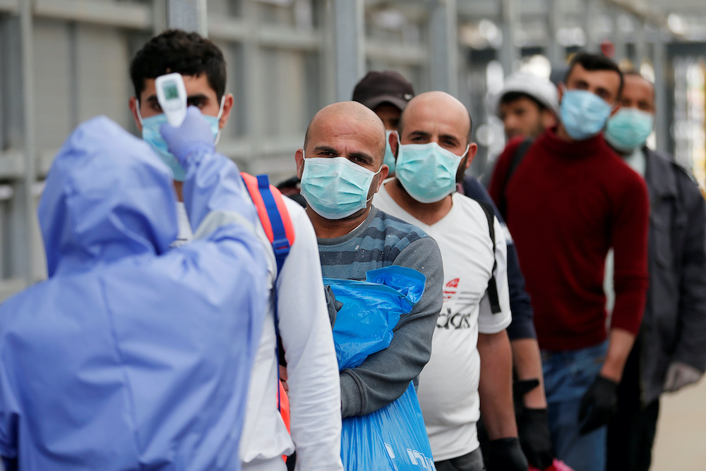 A healthcare worker checks the body temperature of Palestinian workers returning from Israel, amid concerns over the spread of the coronavirus disease (Covid-19), outside the Israeli-controlled Meitar checkpoint, near Hebron in the Israeli-occupied West B