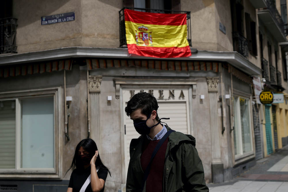 People wearing protective face masks walk past the Spanish flag hanging from the balcony above a closed store amid the coronavirus disease outbreak in Madrid, Spain, April 18, 2020. u00e2u20acu201d Reuters picnn