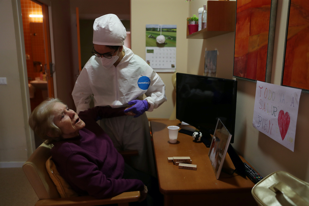 Occupational therapist Teresa Gallego helps resident Esperanza Garcia Bernardos exercise her arm as she stays in her room next to a drawing that reads ‘Everything is going to be fine’  during lockdown amid the coronavirus disease outbreak at Oteruelo 