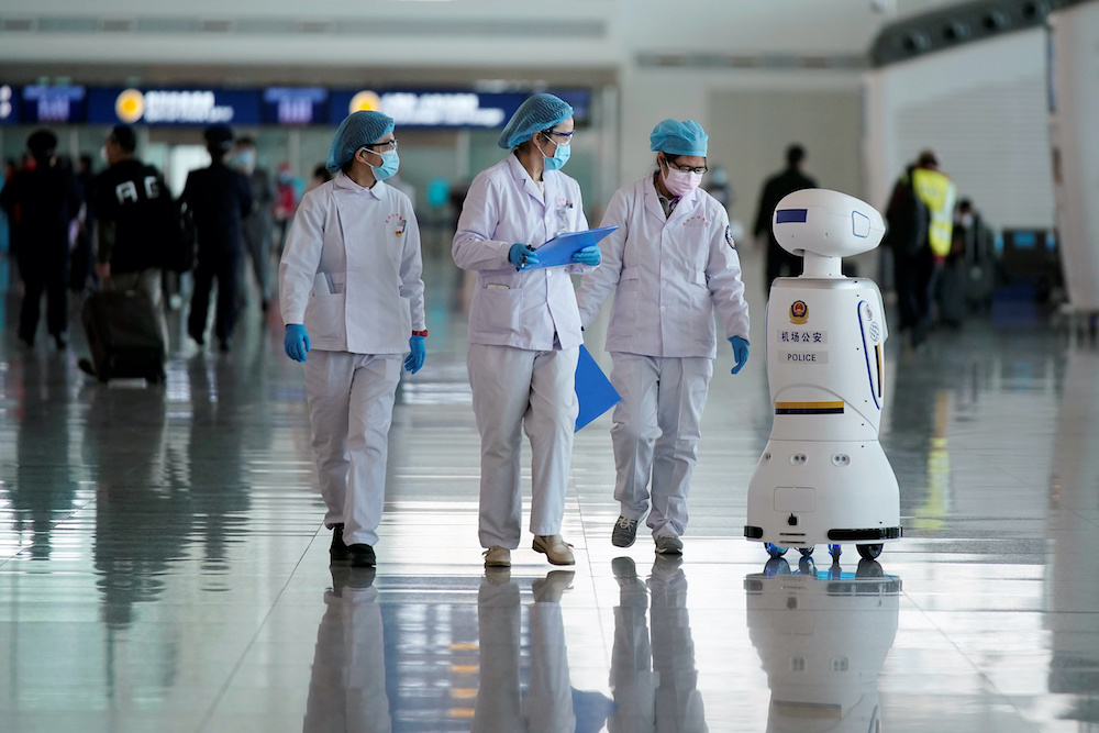 Medical workers walk by a police robot at the Wuhan Tianhe International Airport after travel restrictions to leave Wuhan, the capital of Hubei province and Chinau00e2u20acu2122s epicentre of the novel coronavirus disease (Covid-19) outbreak, were lifted, April 8, 20