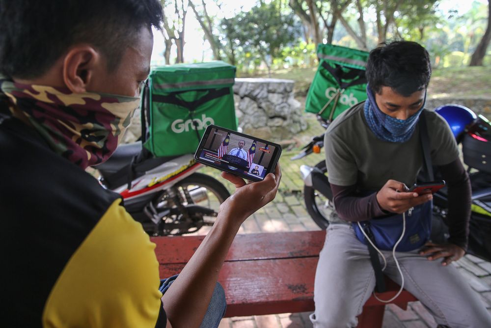 Food delivery rider watching the live telecast of Prime Minister Tan Sri Muhyiddin Yassinu00e2u20acu2122s announcement of a movement control order extension due to the Covid-19 pandemic in Shah Alam, April 10, 2020. u00e2u20acu201d Picture by Yusof Mat Isa