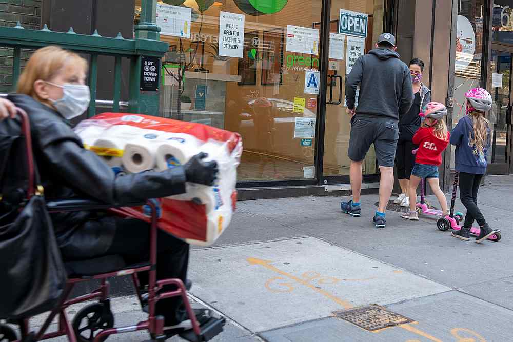 A woman wearing a mask carries toilet paper near a family as the spread of Covid-19 continues in the Manhattan borough of New York April 25, 2020. u00e2u20acu201d Reuters pic