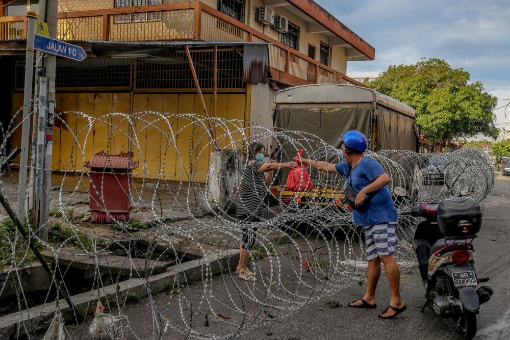 A man is seen passing a bag of groceries through barbed wire fencing to a resident in Selayang Baru, amid the enhanced movement control order April 26, 2020. u00e2u20acu2022 Picture by Firdaus Latif