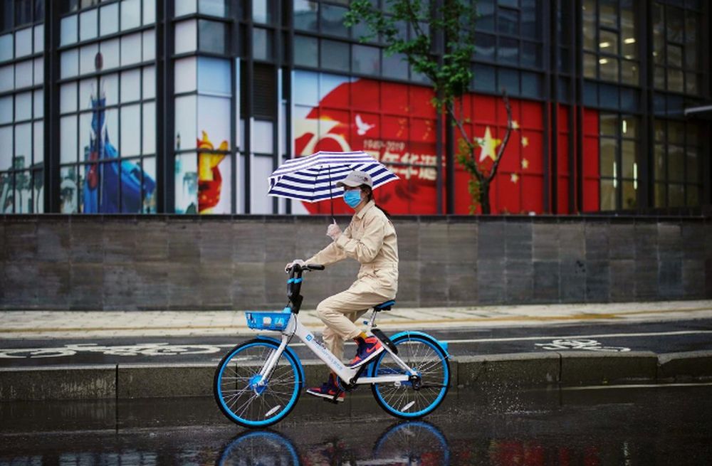 A woman holding an umbrella rides a shared bicycle past an image of the Chinese flag after the lockdown was lifted in Wuhan, Chinau00e2u20acu2122s epicentre of the novel coronavirus disease outbreak, April 10, 2020. u00e2u20acu201d Reuters pic