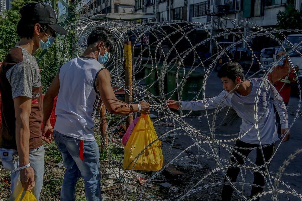 A man is pictured passing bags of groceries through barbed wire fencing to residents in the vicinity of Pasar Borong Kuala Lumpur  amid the enhanced movement control order April 23, 2020. u00e2u20acu2022 Picture by Firdaus Latif