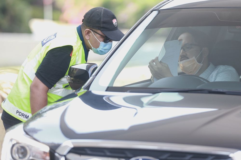 A police personnel inspects a passenger's travel documents  during a roadblock in Petaling Jaya April 1, 2020. u00e2u20acu201d Picture by Ahmad Zamzahuri