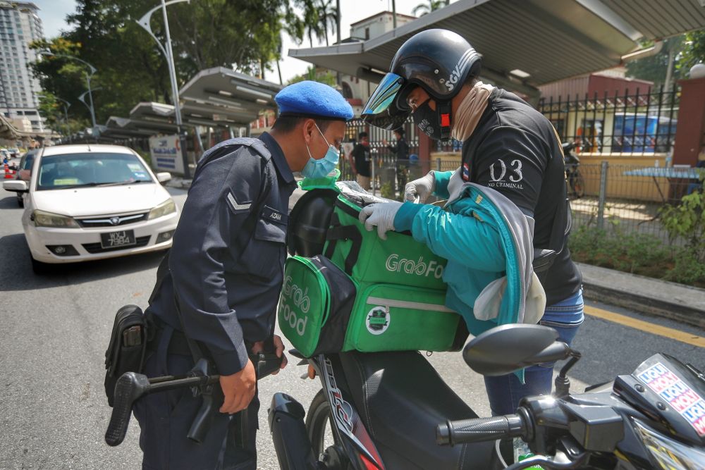 A police personnel conducts checks on a food delivery rider during a road block in Kuala Lumpur April 7, 2020. u00e2u20acu201d Picture by Ahmad Zamzahuri