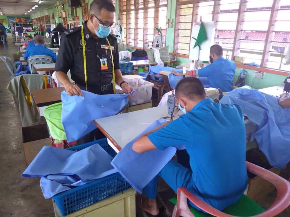 A Kajang Prison inmate sews a PPE suit while his supervisor observes him. u00e2u20acu201d Picture courtesy of Twitter/Malaysian Prisons Department