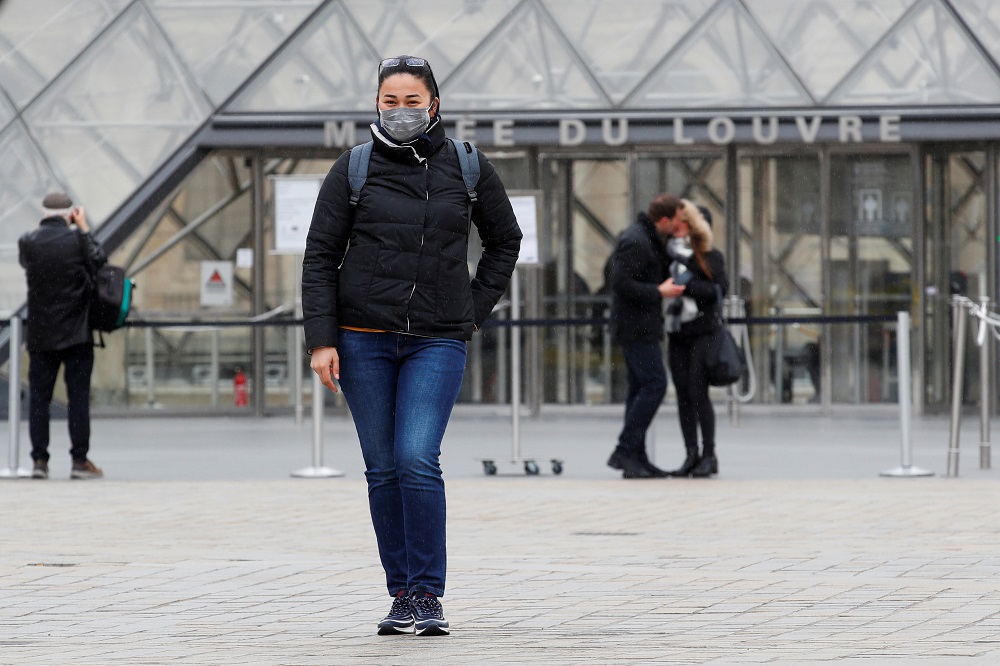 A tourist wearing a protective face mask poses as she stand near The Louvre as the museum among top tourism landmarks closed their doors in Paris March 14,2020. u00e2u20acu201d Reuters pic